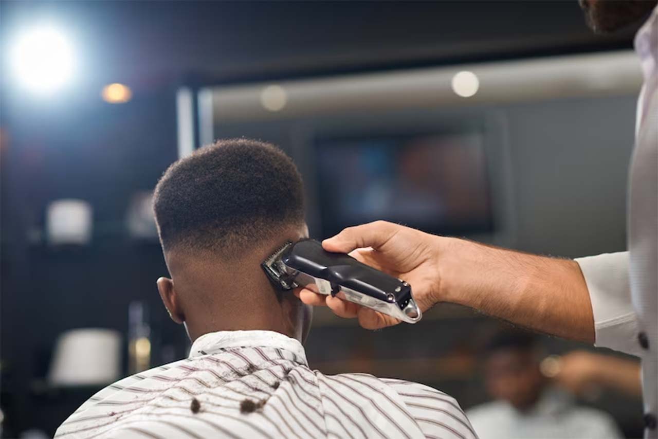Close haircut, barber shaving a man's head. The barber is using an electric codeless shaving machine to shave the man's head. The man is sitting in a barber chair, with his eyes closed and his face relaxed.